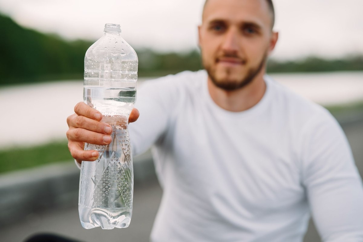 Homme tenant une bouteille d'eau près d'un corps d'eau Homme tenant une bouteille d'eau près d'un corps d'eau