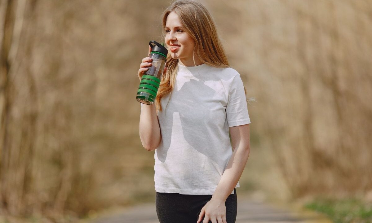 Une femme boit depuis une gourde verte sur un sentier