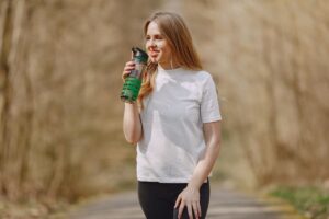Une femme boit depuis une gourde verte sur un sentier
