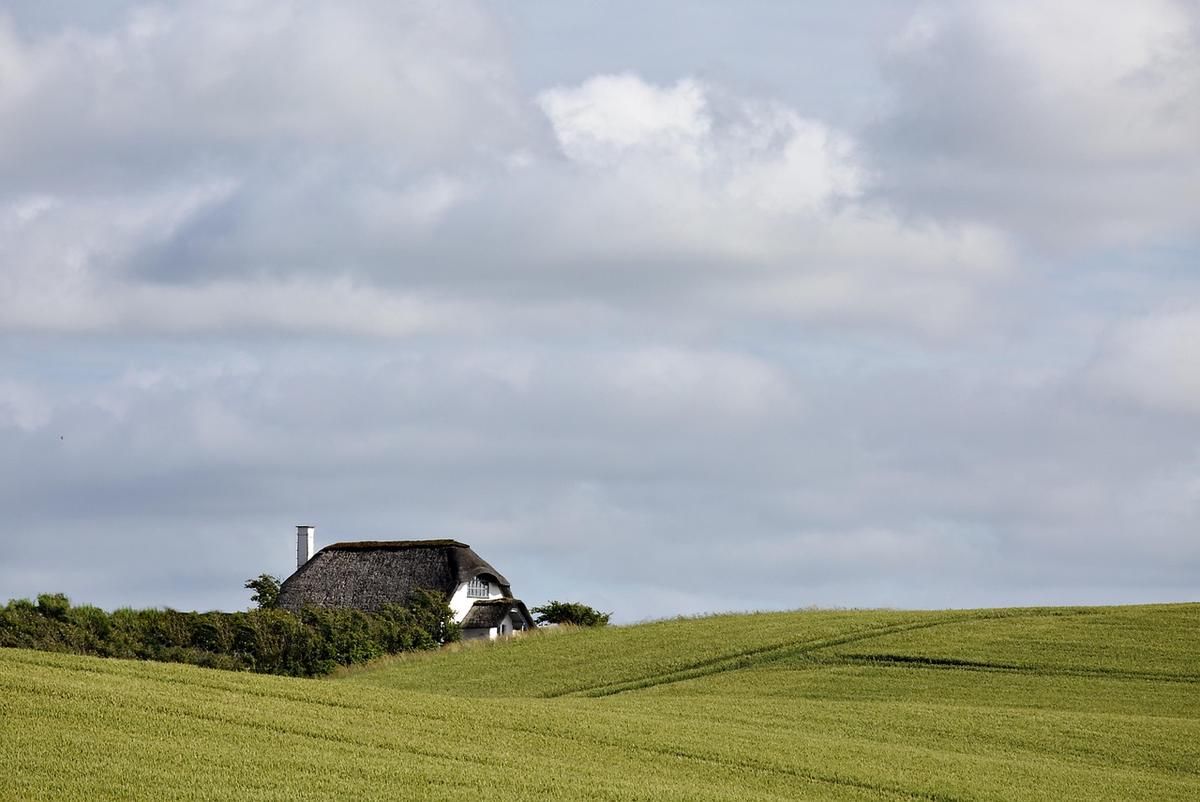 Maison isolée sur une colline, champs étendus, nuages dans le ciel Maison isolée sur une colline, champs étendus, nuages dans le ciel