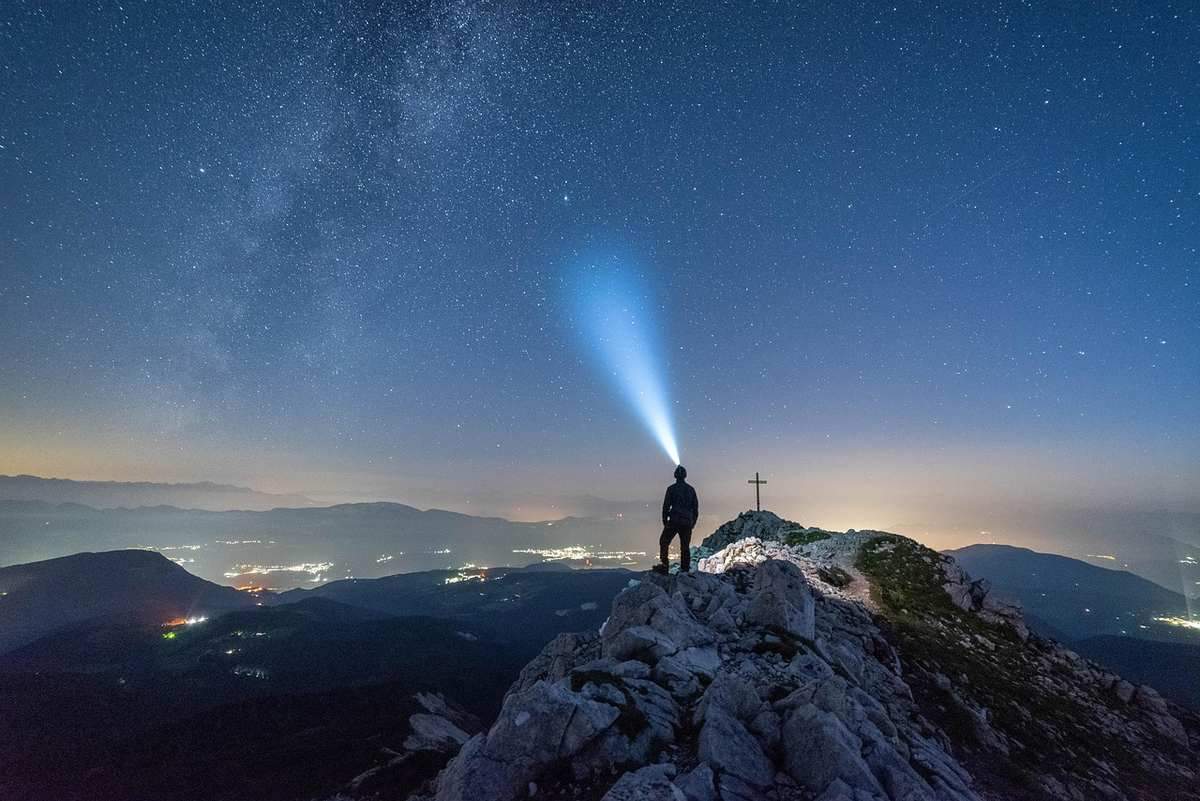Silhouette d'une personne sur une montagne, un phare de lumière dans le ciel nocturne étoilé Silhouette d'une personne sur une montagne, un phare de lumière dans le ciel nocturne étoilé