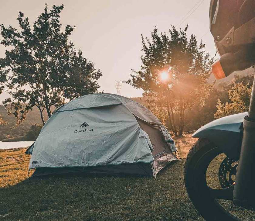 Tente de camping blanche près d'un lac, soleil couchant, moto à l'avant-plan Tente de camping blanche près d'un lac, soleil couchant, moto à l'avant-plan